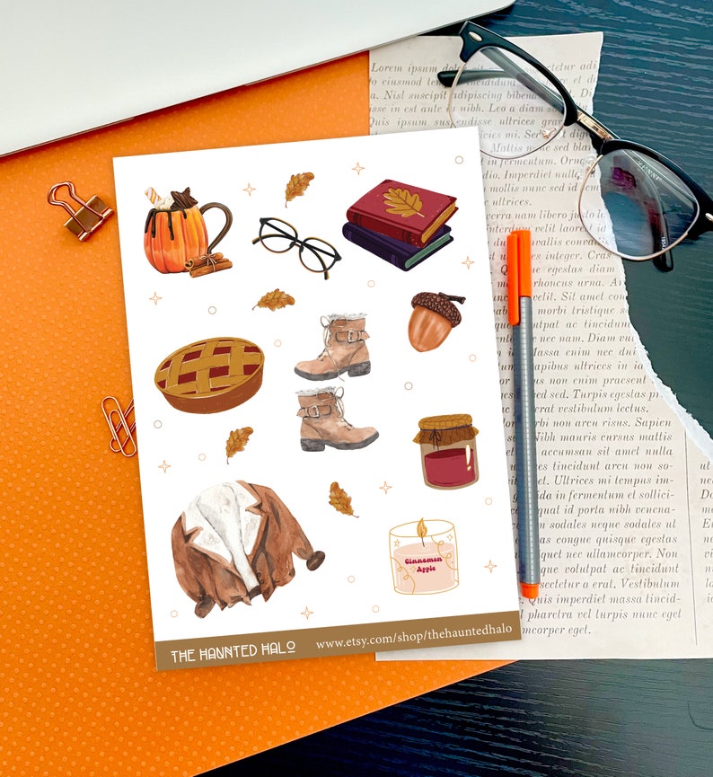 May include: A set of autumn-themed stickers featuring a pumpkin spice latte, a pie, a pair of glasses, boots, a jar of jam, a jacket, a candle, and a stack of books. The stickers are on a white background with a light orange border. The text "THE HAUNTED HALO" and a website address are at the bottom of the sticker sheet.
