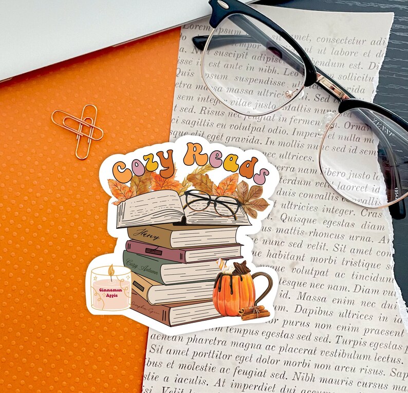May include: Cozy Reads sticker featuring a stack of books, a mug of hot cocoa, a candle, and autumn leaves. The sticker has the text "Cozy Reads" in a retro font.