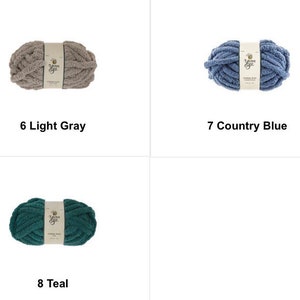 May include: Three skeins of Yarn Bee brand yarn in light gray, country blue, and teal. Each skein is labeled with its color name and number. The yarn appears to be a chunky knit style, perfect for various crafting projects.