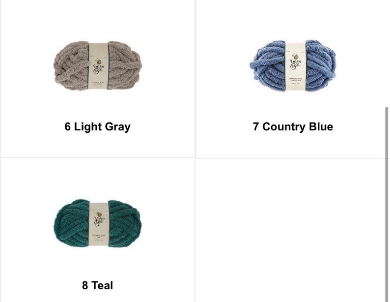 May include: Three skeins of Yarn Bee brand yarn in light gray, country blue, and teal. Each skein is labeled with its color name and number. The yarn appears to be a chunky knit style, perfect for various crafting projects.