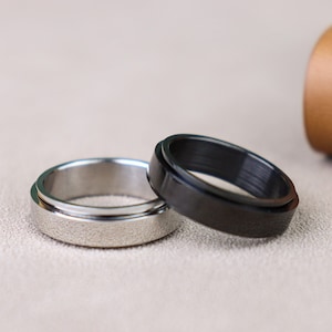 May include: Two spinning rings, one silver and one black, on a light brown surface.