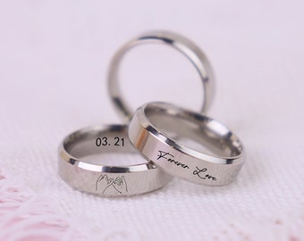 May include: Three silver rings with different engravings. One ring has the inscription "Forever Love", another has the inscription "03.21", and the third has a design of two hands making a pinky promise.