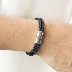 May include: A dark blue braided bracelet with a silver clasp featuring the text "DXN" and a crossed arrow design.