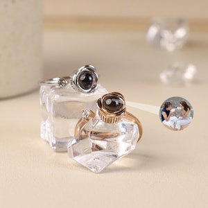 Puede incluir: Dos anillos de plata y oro rosa con un diseño de rosa. Los anillos tienen una pequeña piedra redonda en el centro que parece ser una foto de una pareja.