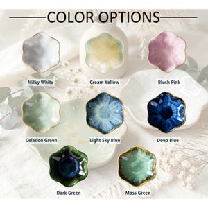 K&ouml;nnte beinhalten: Eine Sammlung von acht kleinen, blumenf&ouml;rmigen Keramikschalen, die mit dem Text COLOR OPTIONS pr&auml;sentiert werden. Die Schalen sind in den Farben Milchwei&szlig;, Cremegelb, Blassrosa, Seladongr&uuml;n, Hellhimmelblau, Tiefblau, Dunkelgr&uuml;n und Moosgr&uuml;n erh&auml;ltlich.