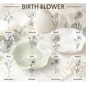 K&ouml;nnte beinhalten: Eine Sammlung von gewellten Keramikschalen mit schwarzen Strichzeichnungen von Geburtsblumen f&uuml;r jeden Monat des Jahres. Der Text BIRTH FLOWER steht oben, zusammen mit Monatsnamen und individuellen Daten wie 05.07.2026.