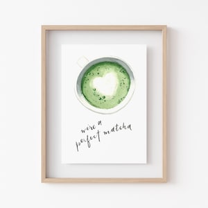 May include: A framed print with a watercolor illustration of a cup of green matcha with a heart-shaped design in the foam. The text "we're a perfect matcha" is written in black cursive below the cup.
