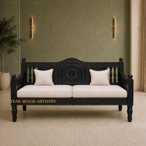 May include: A black wooden sofa with intricate floral carvings on the backrest and frame, featuring two cream-colored rectangular cushions and a cream-colored seat pad. The text "TEAK WOOD ARTISTRY" is printed in gold on the front frame.