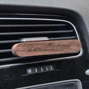 Puede incluir: Un ambientador de coche de madera con el texto "It was all a dream" grabado en él. El ambientador es marrón y tiene una veta de madera natural.