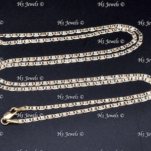 May include: Two gold chains, one longer than the other, with a tri-color design of yellow, white, and rose gold. The chains are made of a box link style. The chains are on a black background.