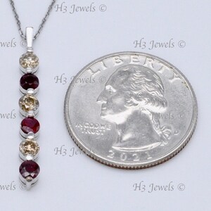 May include: A silver necklace with a pendant featuring a row of alternating red and yellow gemstones. The pendant is about the size of a US quarter.