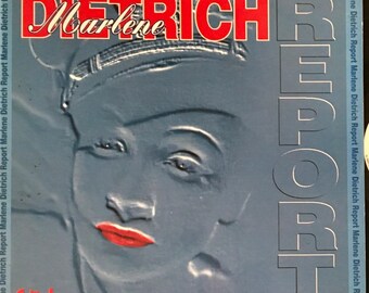 Op de afbeelding: Een blauwe en witte platenhoes met een close-up afbeelding van Marlene Dietrich's gezicht. De albumtitel is "Marlene Dietrich Report" in rode en witte letters.