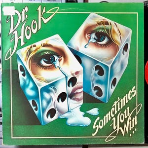 Puede incluir: Una portada de disco de vinilo verde con un diseño de dados azul y blanco. Los dados tienen una cara de mujer en cada lado con una sola lágrima rodando por su mejilla. El texto "Dr. Hook" y "Sometimes You Win..." está escrito en la portada.