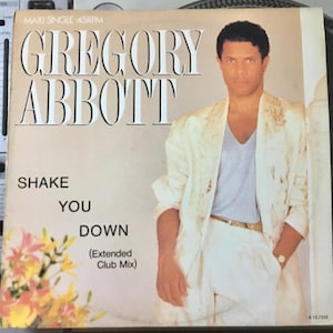 Op de afbeelding: Een witte platenhoes met een foto van een man in een wit jack en een wit shirt. De tekst op de hoes luidt "Gregory Abbott", "Shake You Down" en "(Extended Club Mix)".