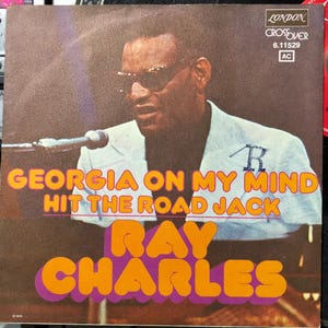 Puede incluir: Portada del álbum con Ray Charles con gafas de sol y un traje claro, cantando a un micrófono. El título del álbum, "Georgia on My Mind" y "Hit the Road Jack", está en texto naranja y morado, con "Ray Charles" debajo.