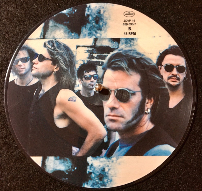 May include: A black and white vinyl record with a photo of a band on the label. The band members are wearing sunglasses and have a rock and roll look. The label text reads "JOVP 15 856 638-7 B 45 RPM".