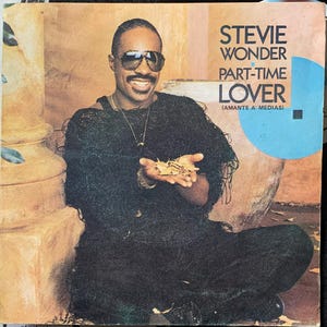 Pode incluir: Capa do álbum com Stevie Wonder sorrindo e segurando folhas. Ele usa óculos de sol e uma roupa escura. O título do álbum é "Part-Time Lover".
