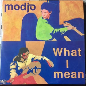 Peut inclure: Une pochette d'album bleue et jaune avec le nom du groupe "modjo" en texte blanc. Le titre de l'album "What I mean" est en texte doré sur fond bleu. La pochette présente deux hommes, l'un jouant de la guitare et l'autre assis à un clavier.