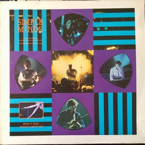 Pode incluir: Uma capa de álbum de vinil com fundo listrado roxo e azul. A capa do álbum apresenta uma banda chamada "Simple Minds" e o texto "The Breakfast Club" trilha sonora. A capa do álbum também apresenta quatro imagens dos membros da banda.