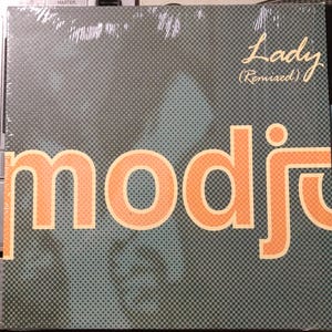 Peut inclure: Un album vinyle avec le mot "modjo" en lettres orange avec un contour blanc. La couverture de l'album a un fond gris avec un motif de points et les mots "Lady (Remixed)" en cursive.