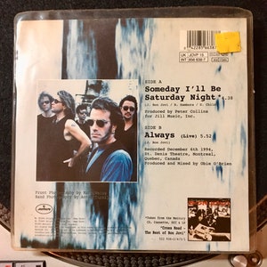 May include: A black and white photo of a band on the back of a CD single. The band is standing in front of a white background. The CD single is for the song "Someday I'll Be Saturday Night" by Bon Jovi. The text "Always (Live)" is also on the back of the CD single.