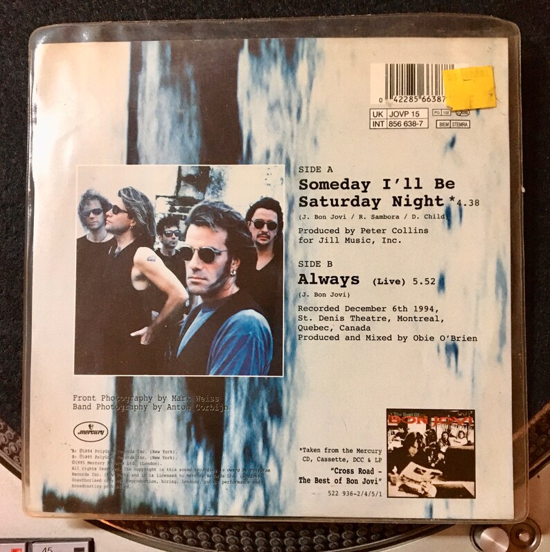 May include: A black and white photo of a band on the back of a CD single. The band is standing in front of a white background. The CD single is for the song "Someday I'll Be Saturday Night" by Bon Jovi. The text "Always (Live)" is also on the back of the CD single.