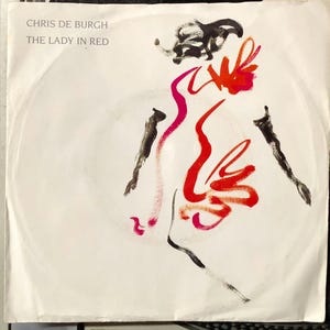 May include: A white record label with black text that reads "Chris de Burgh" and "The Lady in Red". A black and red abstract illustration of a person in a red dress is in the centre of the label.
