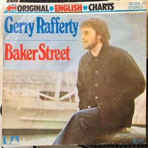 May include: A vintage vinyl record sleeve for Gerry Rafferty's "Baker Street." The cover displays the artist's name in blue and the song title in red against a blue and white backdrop. A man in a dark jacket and jeans is pictured.