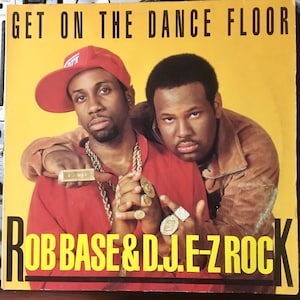May include: A yellow record cover with the text "GET ON THE DANCE FLOOR" in black letters. Two men are pictured on the cover, one wearing a red shirt and a red baseball cap, the other wearing a brown jacket. The text "ROB BASE & DJ E-Z ROCK" is in yellow letters at the bottom of the cover.