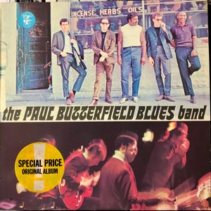 Puede incluir: Una portada de álbum de vinilo vintage con una banda llamada "the PAUL BUTTERFIELD BLUES band". La portada muestra a cinco hombres de pie frente a un edificio con un letrero que dice "INCENSE, HERBS, OILS". La portada del álbum también incluye una pegatina amarilla que dice "SPECIAL PRICE ORIGINAL ALBUM".