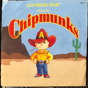 Puede incluir: Una portada de disco de vinilo con Alvin y las Ardillas. El arte de la portada muestra a Alvin, la ardilla principal, vestido de vaquero con un sombrero rojo y una camisa amarilla. El texto en la portada dice "Achy Breaky Heart" y "Alvin & The Chipmunks".