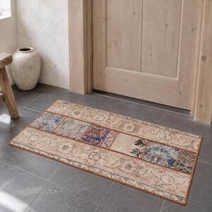 May include: A rectangular area rug featuring a patchwork design with muted beige, blue, and brown tones. The rug displays a variety of faded floral and geometric patterns across its surface, finished with a thin, solid-colored border.