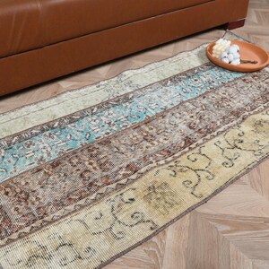 May include: A rectangular area rug featuring a patchwork design with horizontal bands of faded turquoise, brown, and cream colors. The rug displays intricate floral and geometric patterns throughout, with a distressed texture and visible worn edges.