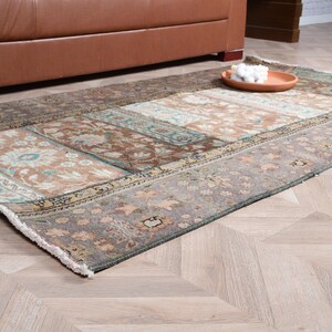 May include: A rectangular area rug featuring a patchwork design with various floral and geometric patterns in muted shades of brown, gray, beige, and teal. The rug has a low pile texture and finished edges with short white fringe on the ends.