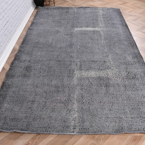 Puede incluir: Una alfombra gris con un patrón sutil. La alfombra tiene un aspecto desgastado y está hecha de un material suave y tejido.