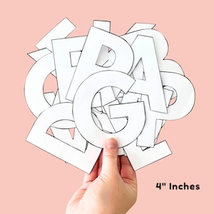 Può includere: Una mano che tiene una collezione di lettere bianche ritagliate su uno sfondo rosa chiaro. Le lettere sono alte circa 10 cm. Le lettere sono in vari stili e caratteri.