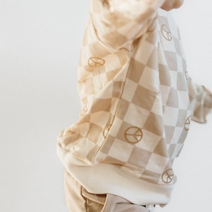 Puede incluir: Una sudadera de color beige y crema a cuadros con gr&aacute;ficos de signo de paz. La sudadera tiene un dobladillo y pu&ntilde;os de canal&eacute;.