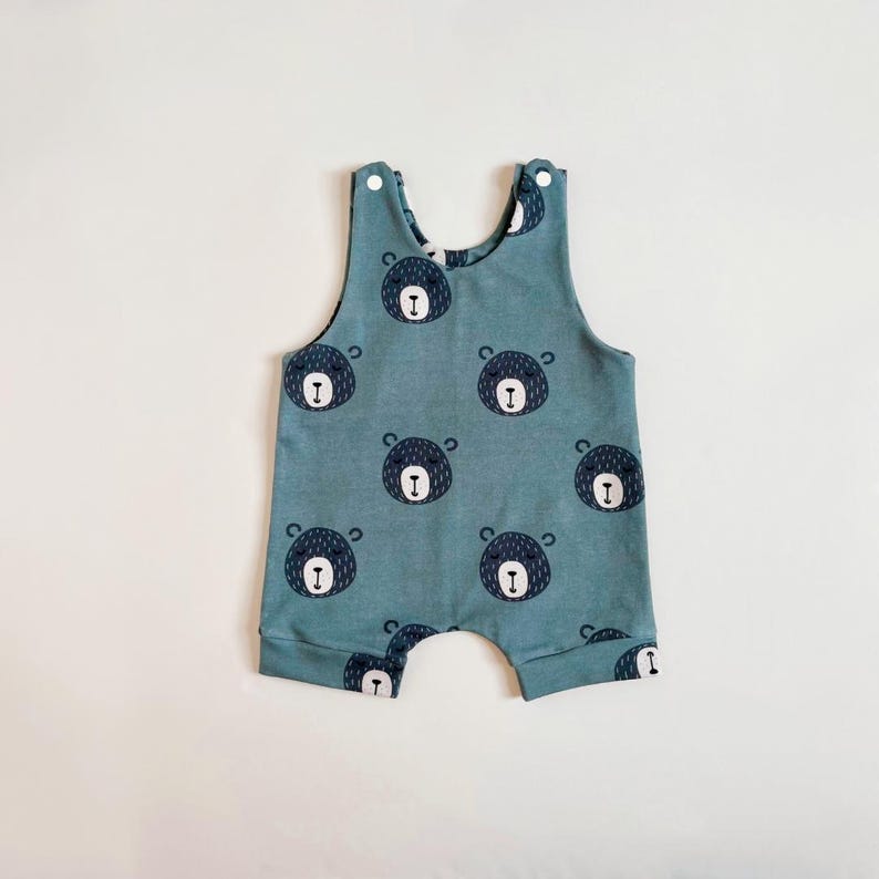 May include: A blue baby onesie with a bear print all over. The onesie has a sleeveless design and a snap closure at the crotch.
