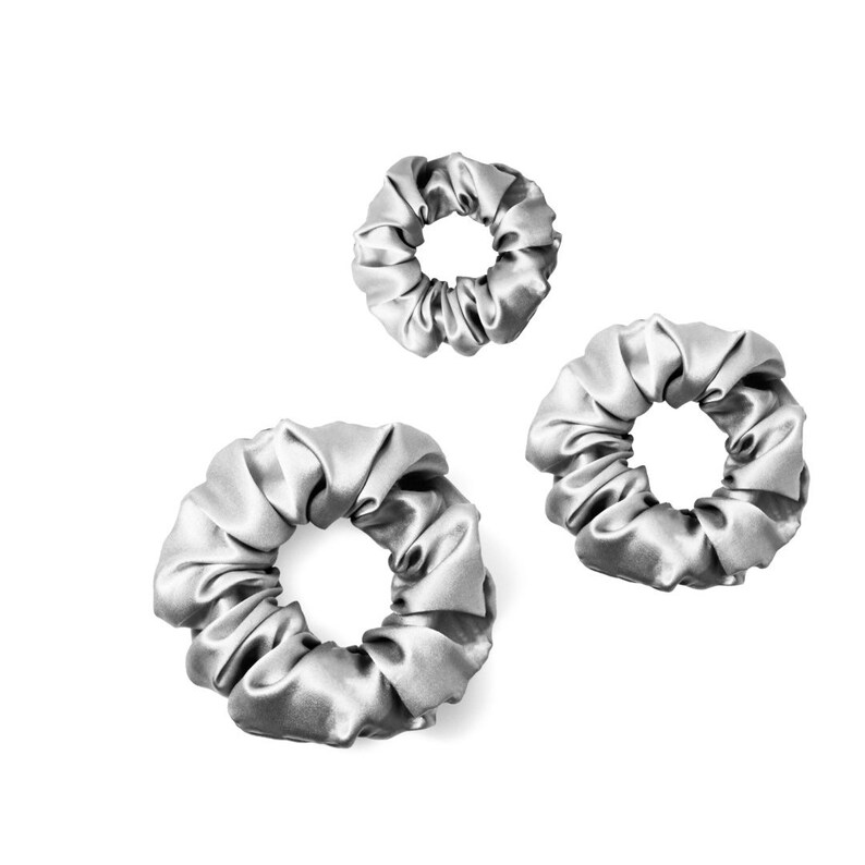 Pu&ograve; includere: Tre scrunchies di raso argentato di diverse dimensioni. Gli scrunchies sono realizzati in tessuto morbido e setoso e sono perfetti per tenere i capelli in posizione.