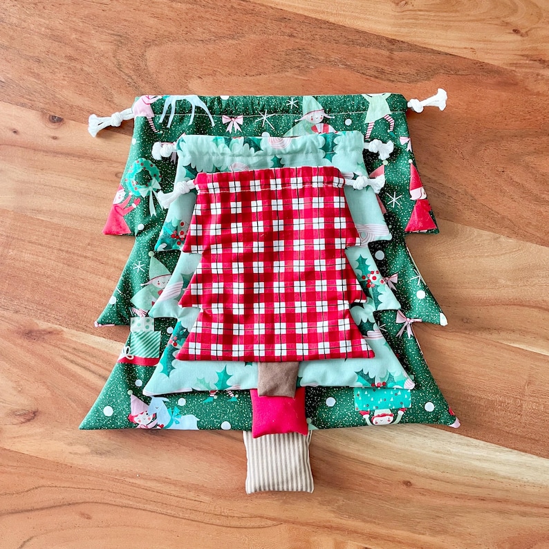 May include: A handmade Christmas tree made of fabric pouches in various sizes and patterns. The tree features green, red, and blue fabrics with holiday-themed prints. The tree is arranged on a wooden surface.
