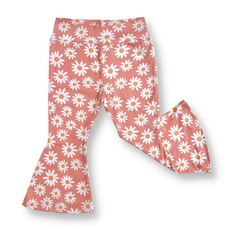 May include: A pair of pink bell bottom pants with a white daisy print. The pants have a wide leg opening and a high waist.