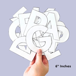 May include: A hand holding a collection of white paper letters against a light purple background. The letters are outlined in black and appear to be cut out. The text "6" Inches" is visible in the image.