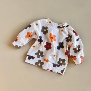 Puede incluir: Sudadera blanca con un estampado floral colorido. Las flores son en tonos de marr&oacute;n, naranja y crema.