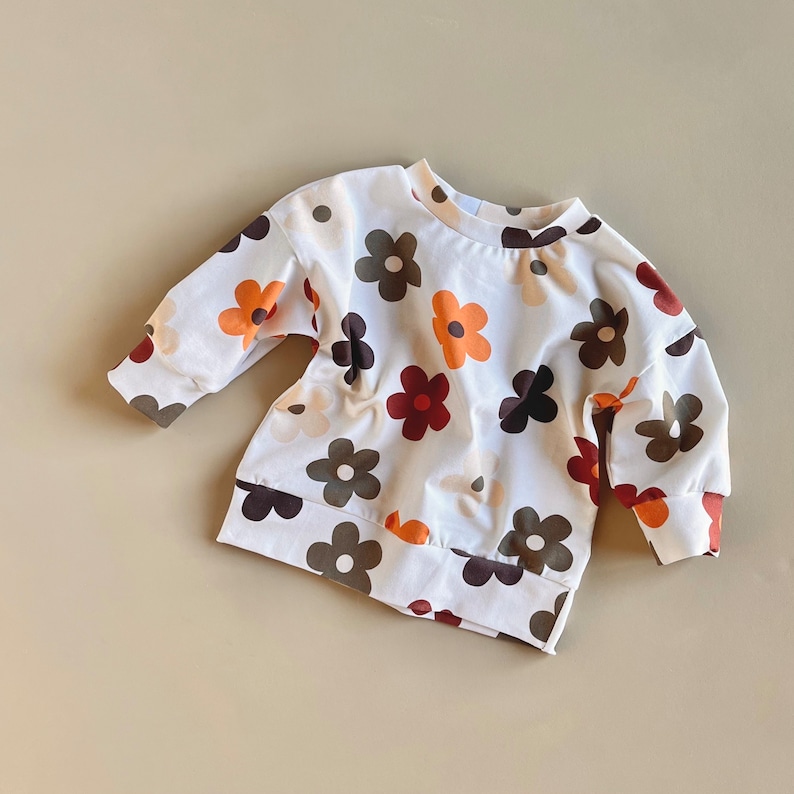 Puede incluir: Sudadera blanca con un estampado floral colorido. Las flores son en tonos de marr&oacute;n, naranja y crema.