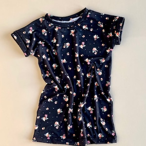 K&ouml;nnte beinhalten: Ein schwarzes T-Shirt mit kurzen &Auml;rmeln und einem kleinen Blumenmuster. Das Shirt hat einen runden Ausschnitt und aufgerollte &Auml;rmel.