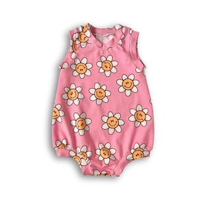 Op de afbeelding: Roze baby romper zonder mouwen met een witte en gele print van glimlachende madeliefjes.