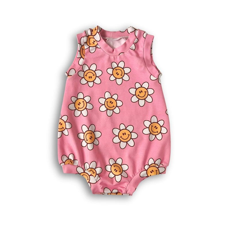 Op de afbeelding: Roze baby romper zonder mouwen met een witte en gele print van glimlachende madeliefjes.