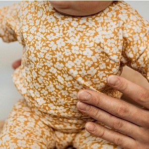 May include: A baby wearing a yellow and white floral print short-sleeve top and matching pants.