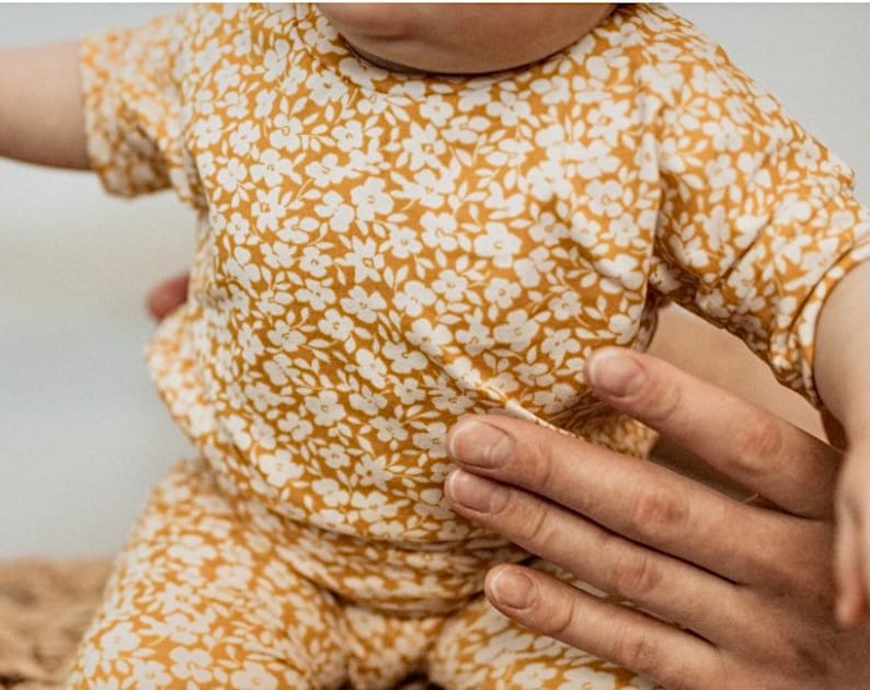 May include: A baby wearing a yellow and white floral print short-sleeve top and matching pants.