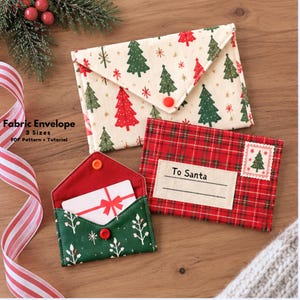 May include: Three fabric envelopes featuring Christmas designs. One cream envelope has red and green trees, one red plaid envelope is labeled To Santa with a tree stamp, and one green envelope with white sprigs holds a white card with a red bow.